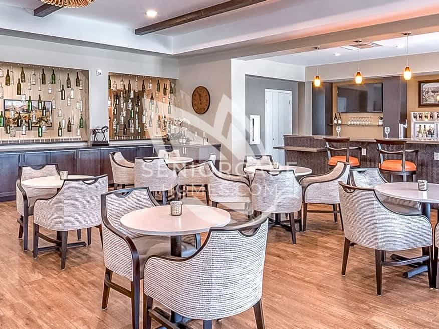 Bistro and wine bar at Clearwater at Sonoma Hills with a lighted wine bottle display, round tables, and orange bar stools.
