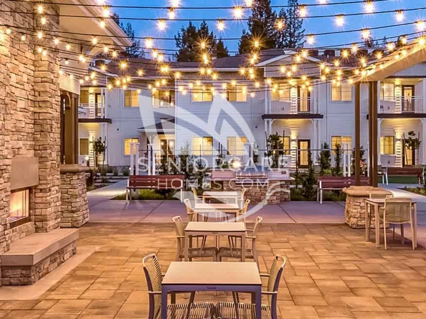 Courtyard patio at Clearwater at Sonoma Hills at dusk, with string lights overhead, a stone fireplace, an outdoor grill, and patio tables.