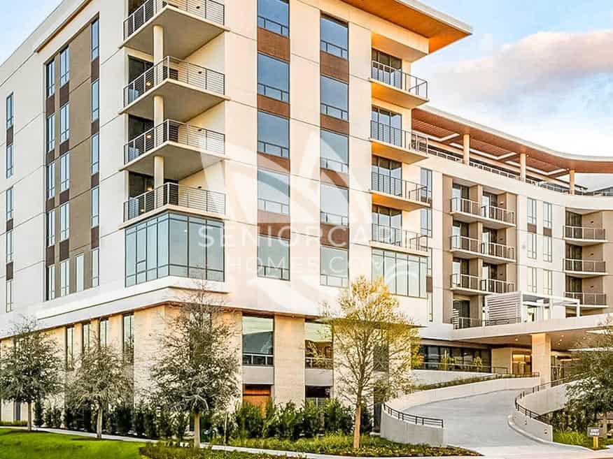 Exterior of Clearwater at The Heights, a modern seven-story senior living building with cream walls, wood-tone accents, private balconies, and a curved driveway.