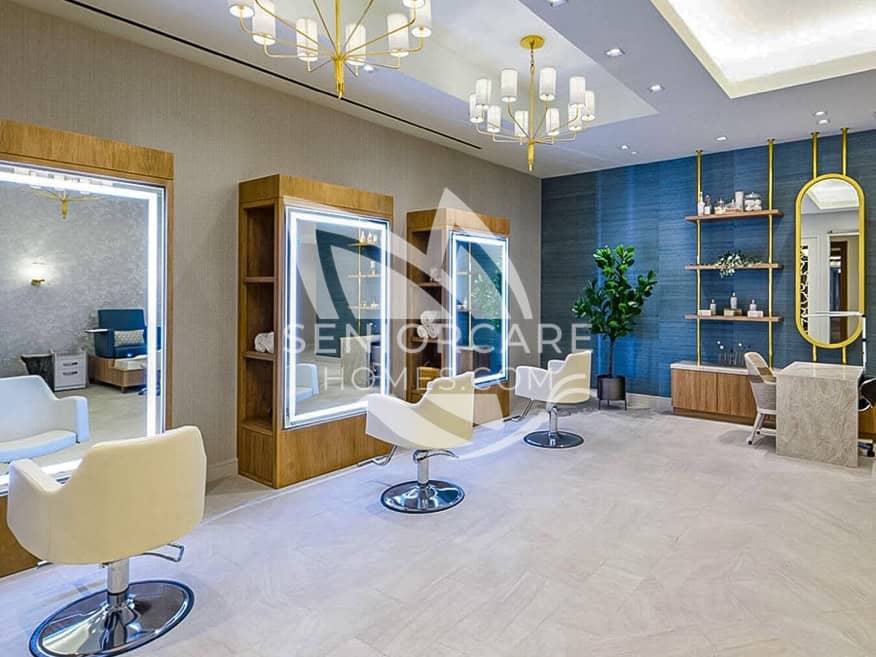 On-site beauty salon at Clearwater at The Heights with white styling chairs, lighted mirrors, a blue accent wall, and gold chandeliers.