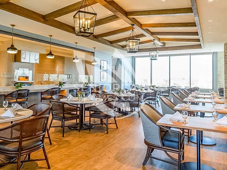Casual dining room at Clearwater at The Heights with wood beam ceilings, lantern-style lights, and an open kitchen with a pizza oven.