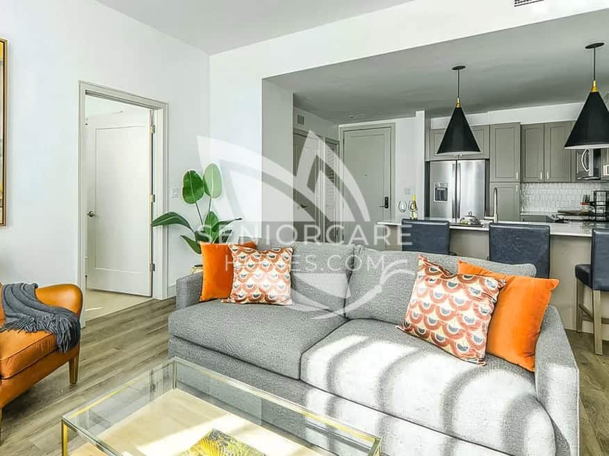 Furnished apartment at Clearwater at The Heights with a gray sofa, orange accent pillows, and an open kitchen with stainless steel appliances.