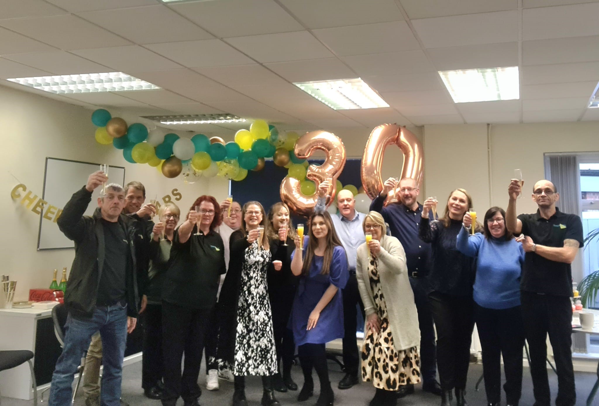Group of colleagues celebrating 30th anniversary with balloons and cheers.