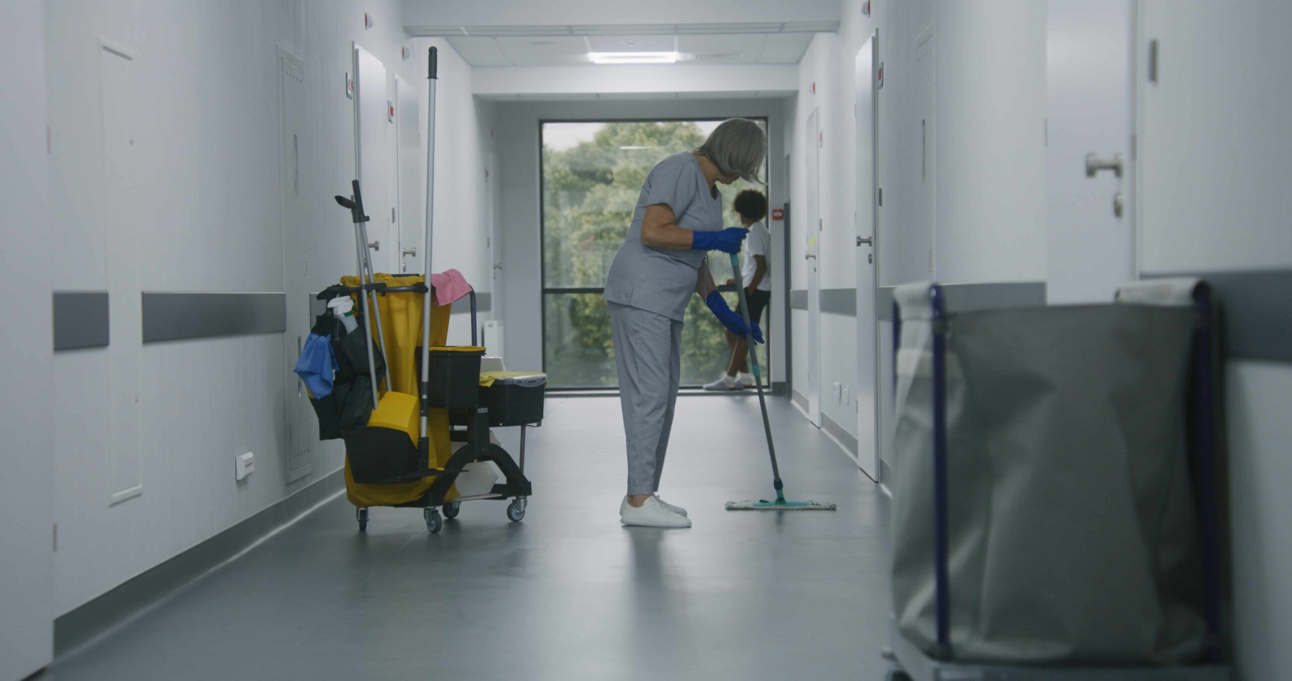 A hospital corridor being cleaned by a staff member with cleaning equipment.