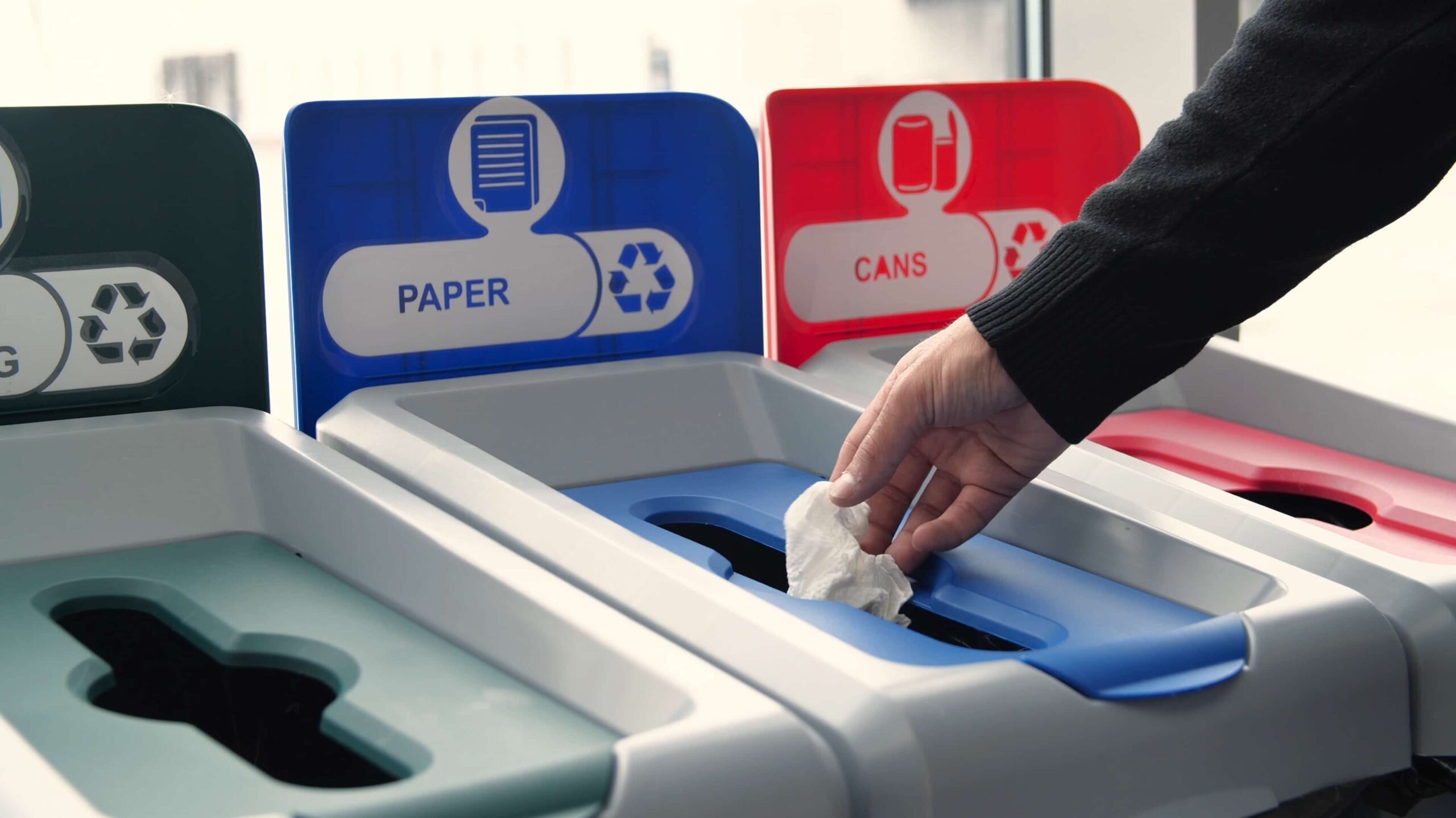 Recycling bins for paper, cans, and general waste in a public space.