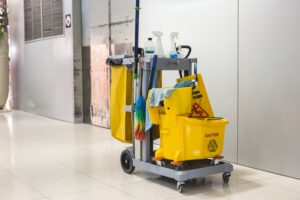 A cleaning cart equipped with mops, sprays, and a caution sign, used for professional cleaning services