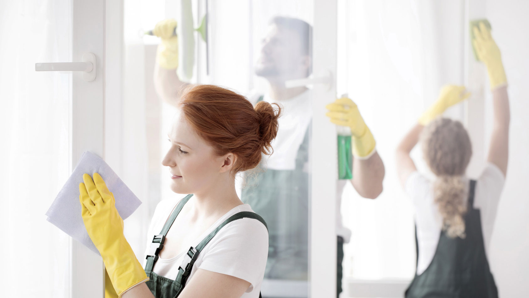 Woman cleaning window with yellow gloves and cloth in brightsetting.
