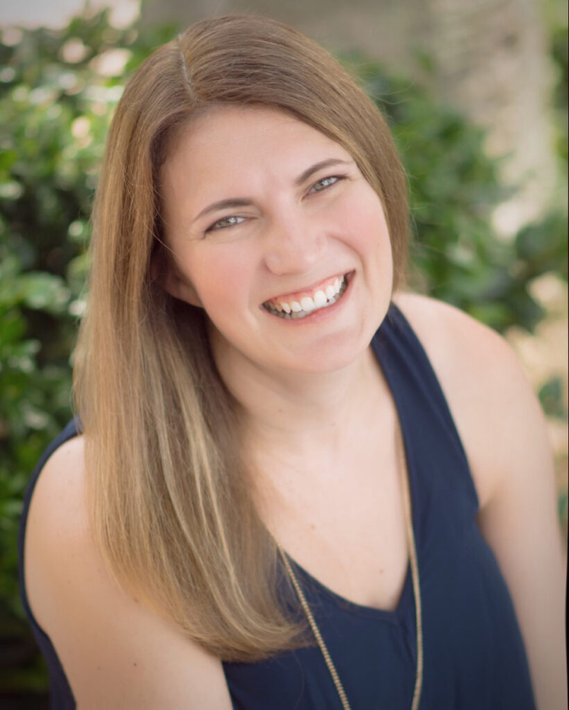 A smiling woman named Shelley Tomich with long, straight hair, wearing a sleeveless navy top, is photographed outdoors with greenery in the background; she exudes confidence as a successful teacherpreneur.
