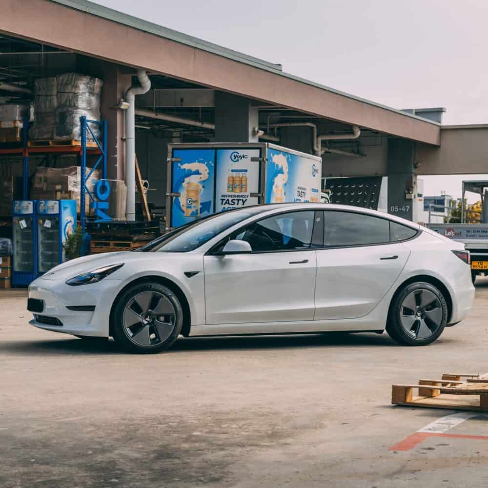 Tesla Model 3 electric vehicle charging at a station in an industrial setting.