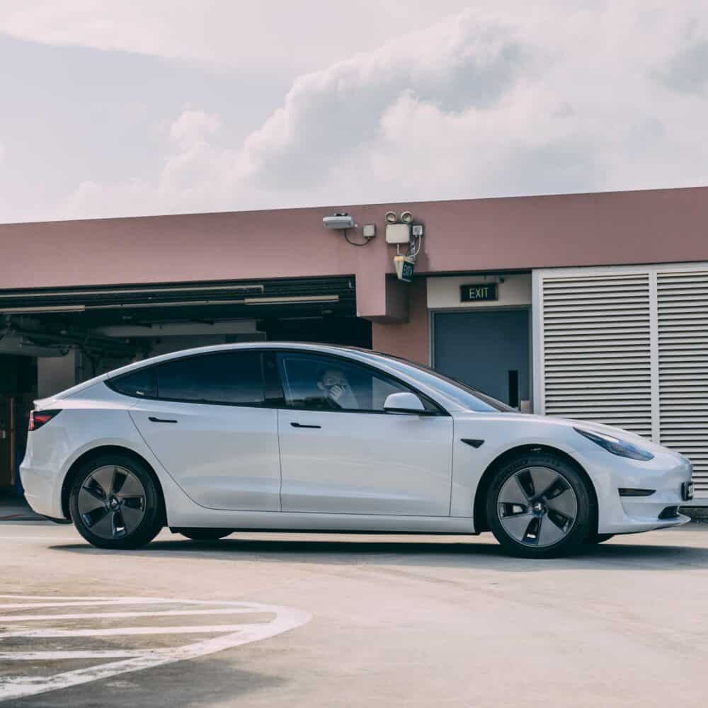 Tesla Model 3 electric vehicle in sleek white color, parked outdoors near a commercial building.