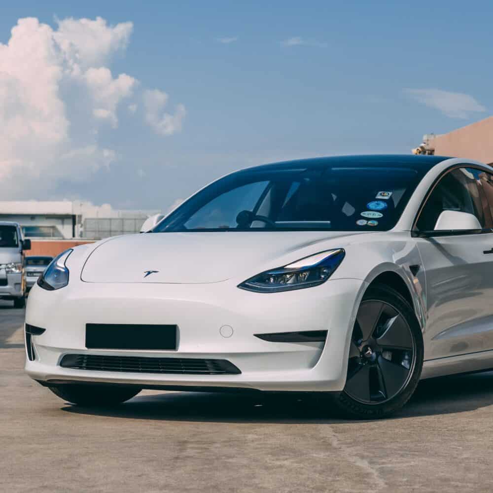 White Tesla Model 3 electric vehicle on parking lot with blue sky.