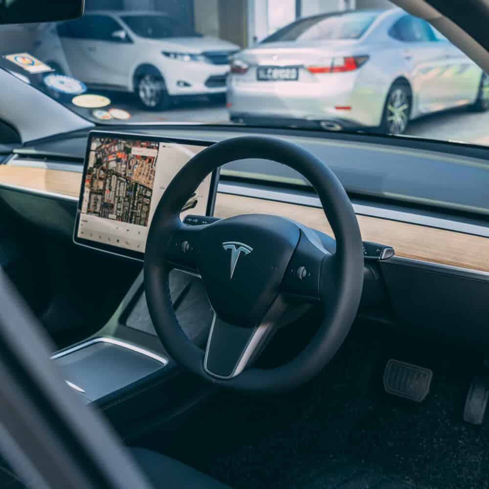Tesla electric vehicle interior with steering wheel and navigation screen.