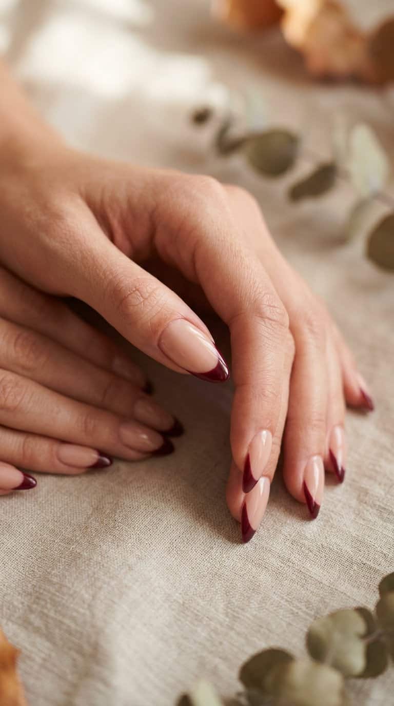 A hand displaying almond-shaped nails with burgundy French tips.