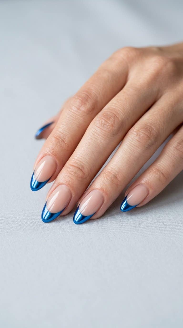 A hand displaying almond-shaped nails with sheer nude bases and electric blue chrome French tips.