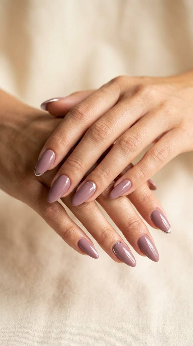 A hand with mauve almond-shaped nails featuring subtle chrome accents.