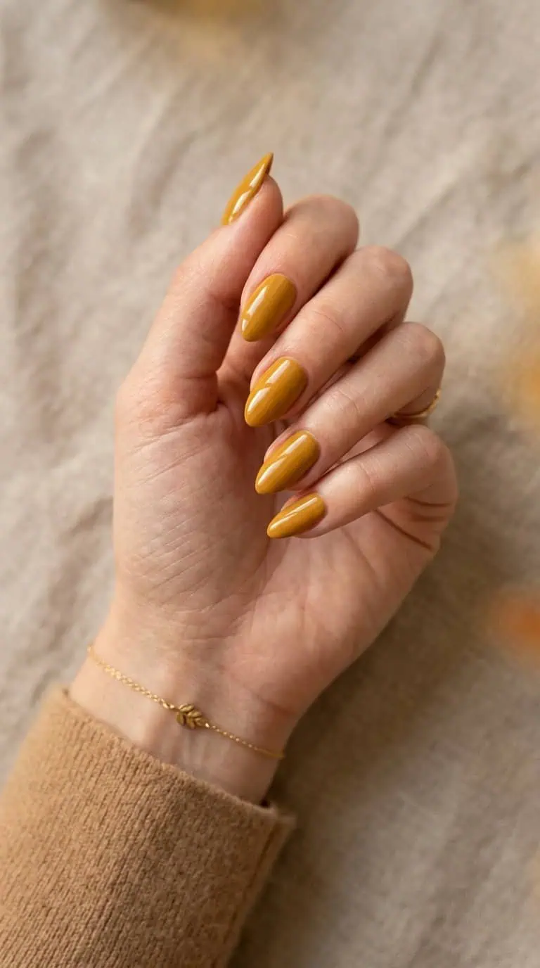 A hand with glossy mustard yellow almond-shaped nails against a neutral background.