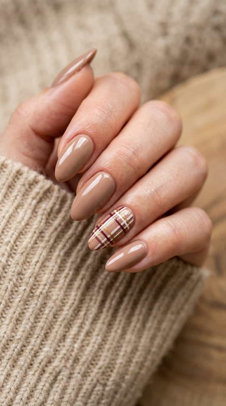 A hand with almond-shaped nails featuring warm autumn colors and plaid accent designs.