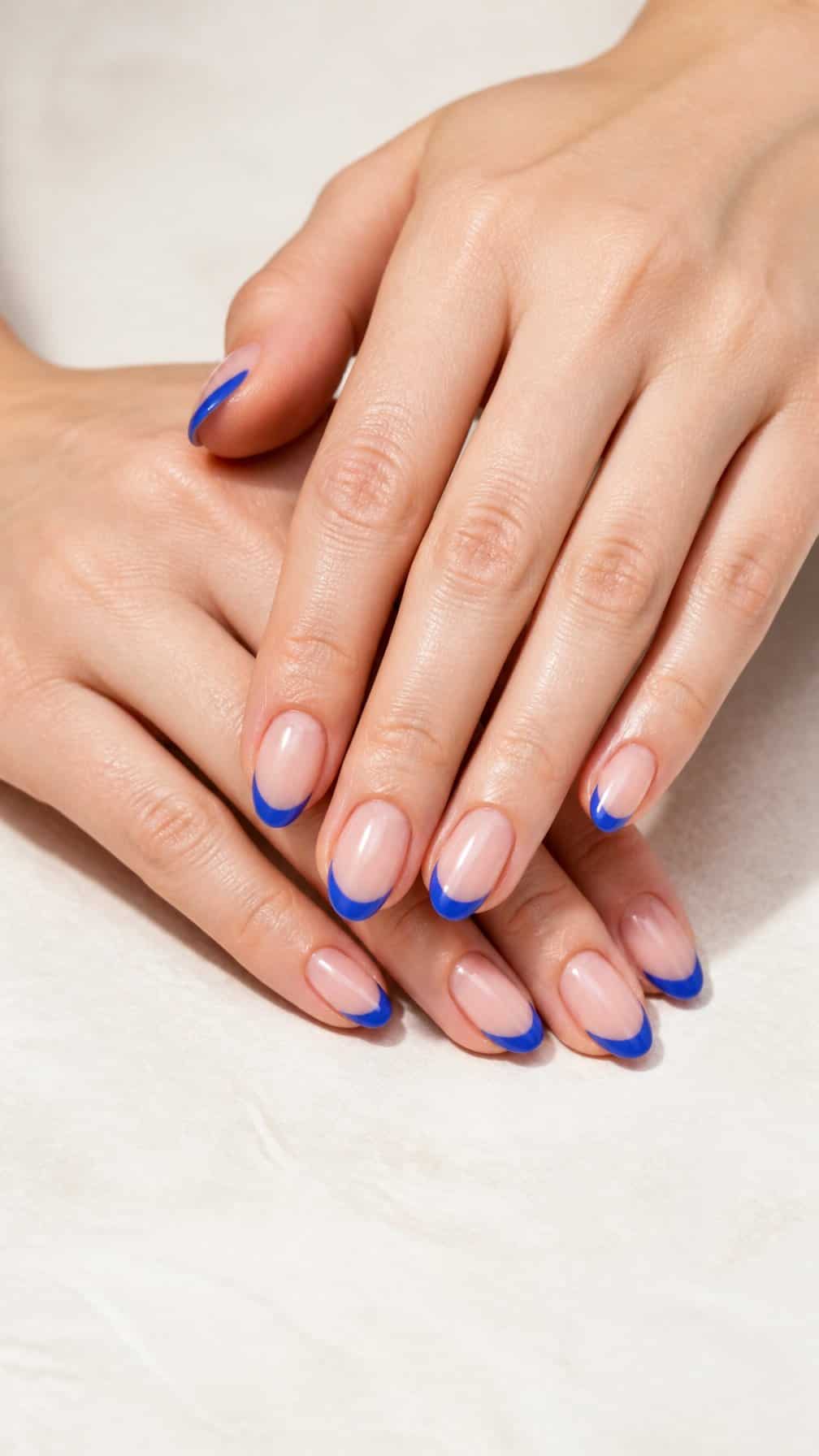 A close-up of hands with nude nails featuring blue French tips.