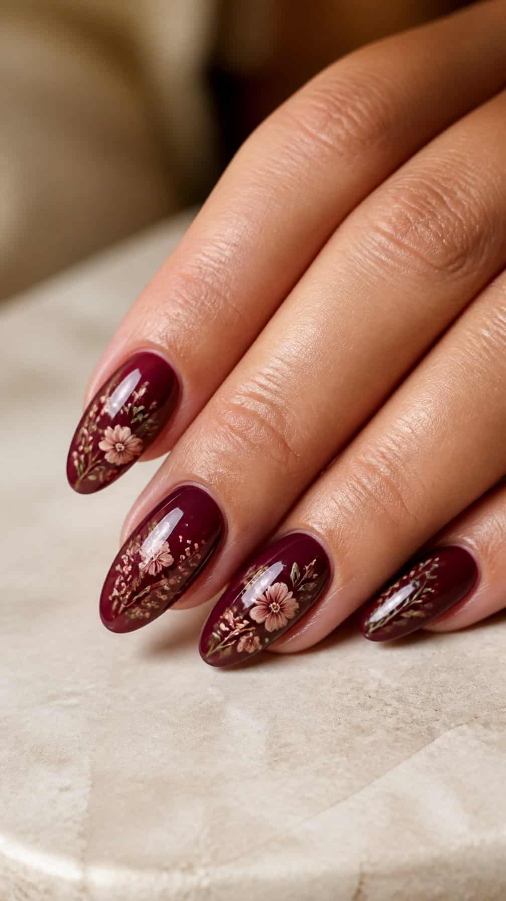 A close-up of a hand with burgundy floral nail art on almond-shaped nails.