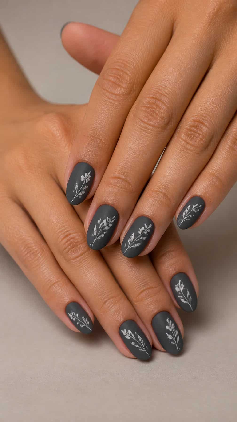 Hands displaying charcoal gray nails with delicate white floral designs.