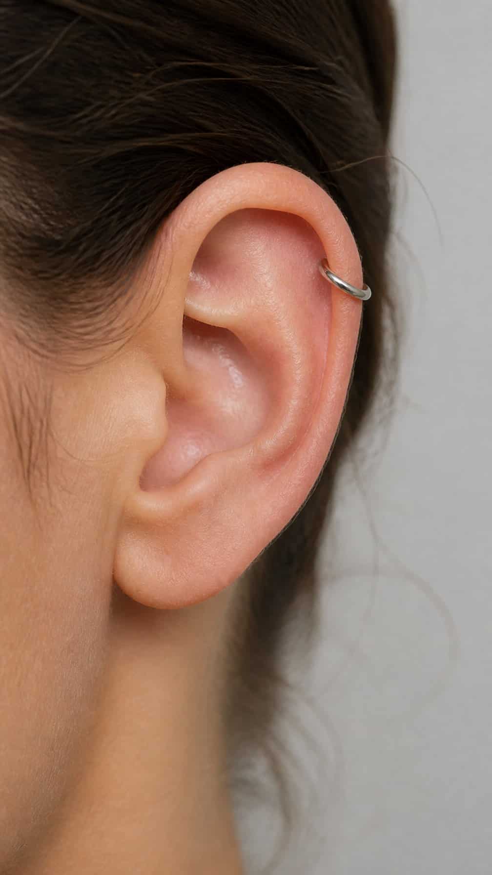 Close-up of an ear wearing a simple titanium hoop in the upper cartilage.