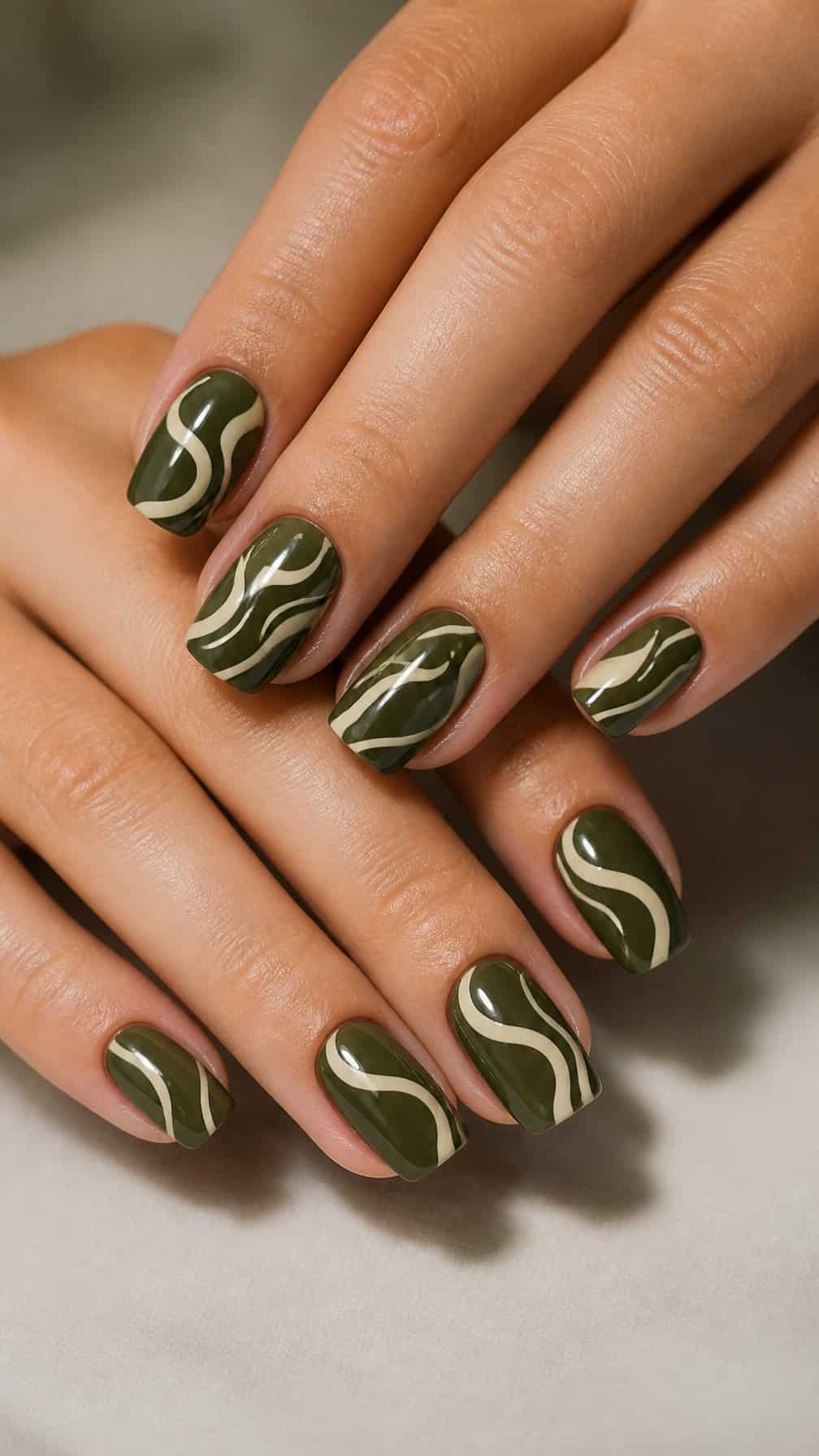Close-up of manicured hands with dark olive nails decorated with cream swirls.