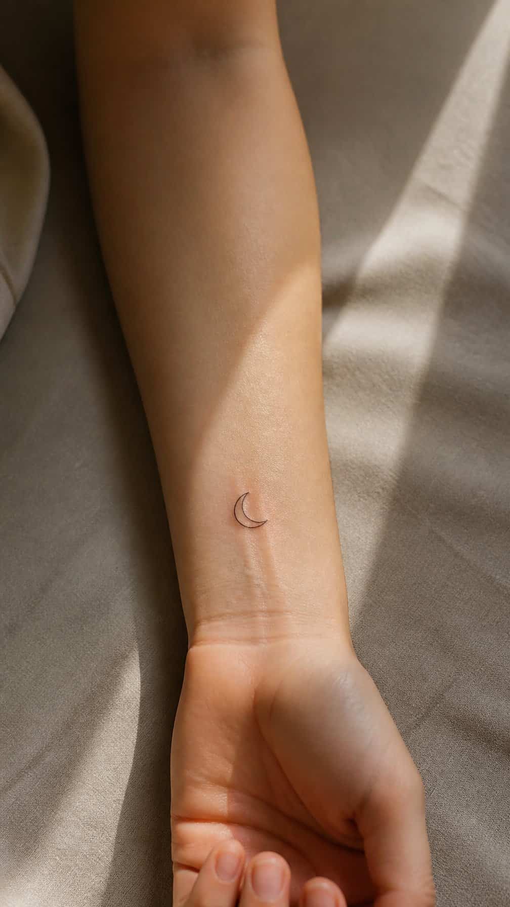 A small crescent moon tattoo on a person's inner forearm.