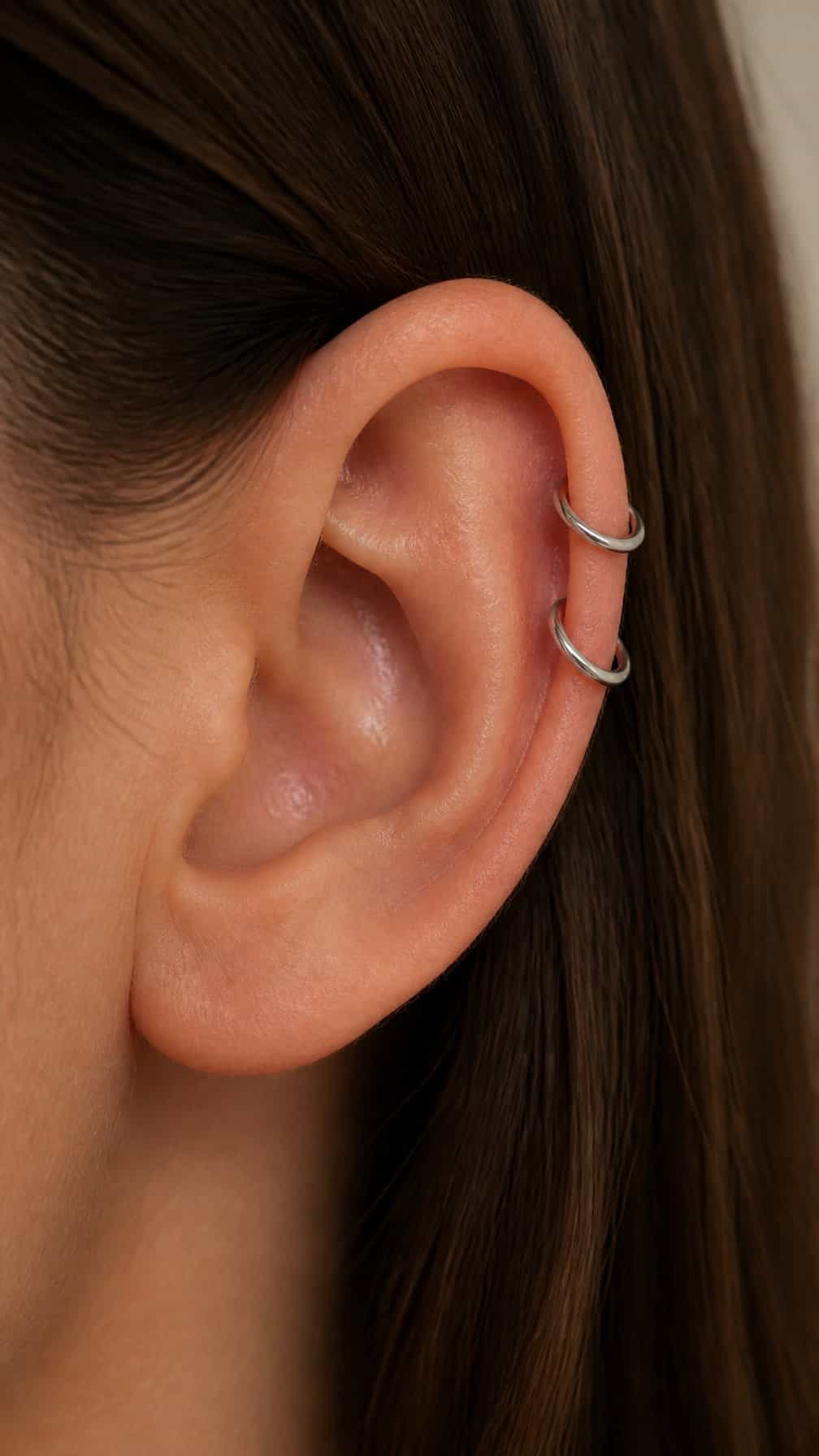 Close-up side view of an ear with two graduated hoop piercings along the upper cartilage.