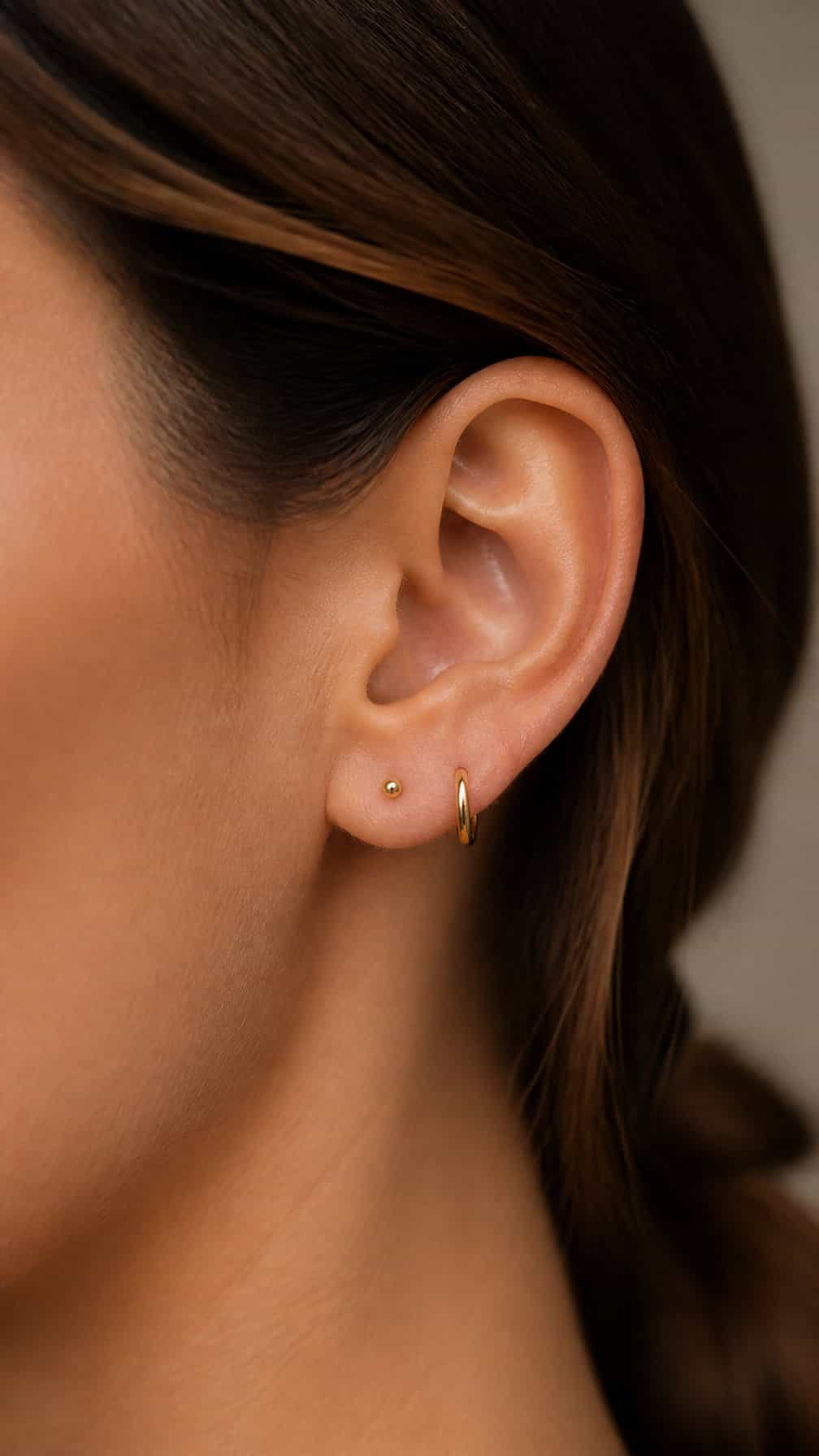 Close-up of an ear with two aligned lobe piercings, including a tiny gold hoop.