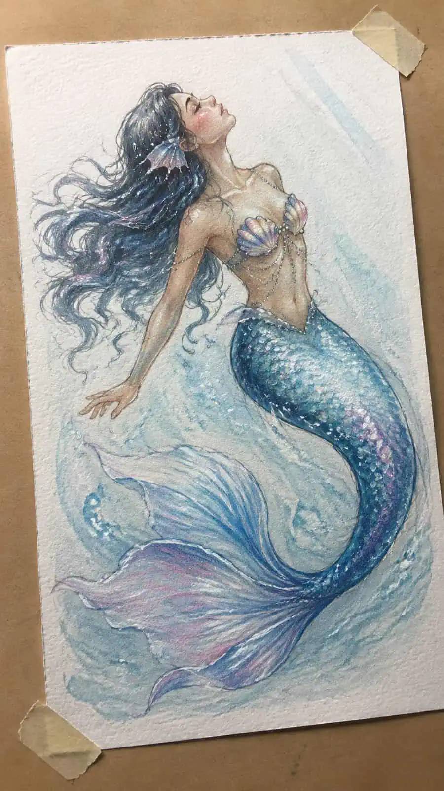 Hand-drawn glistening mermaid tale in colored-pencil and gouache drawing on textured paper, shown in a gentle oblique desk view that — study 3