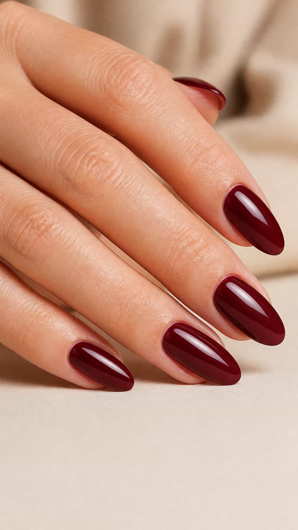 A hand with glossy burgundy almond-shaped nails resting on a neutral surface.