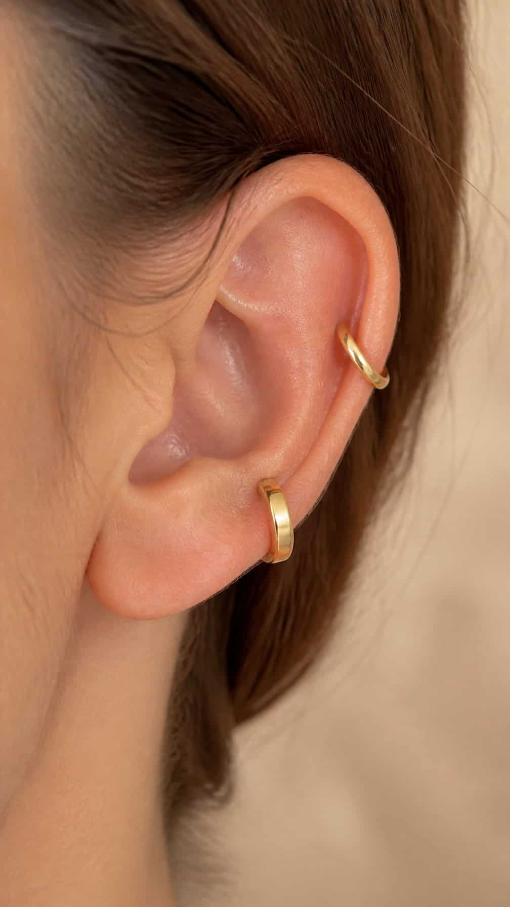 Close-up of an ear with a high helix piercing and a small huggie hoop.