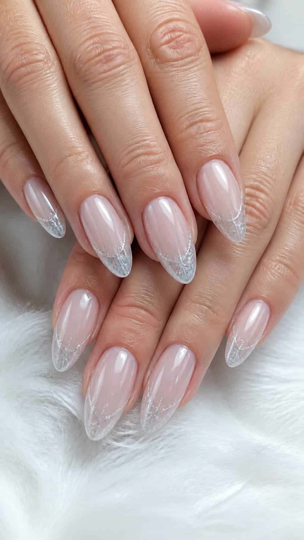A close-up of almond-shaped nails with translucent bases and frosty white French tips.