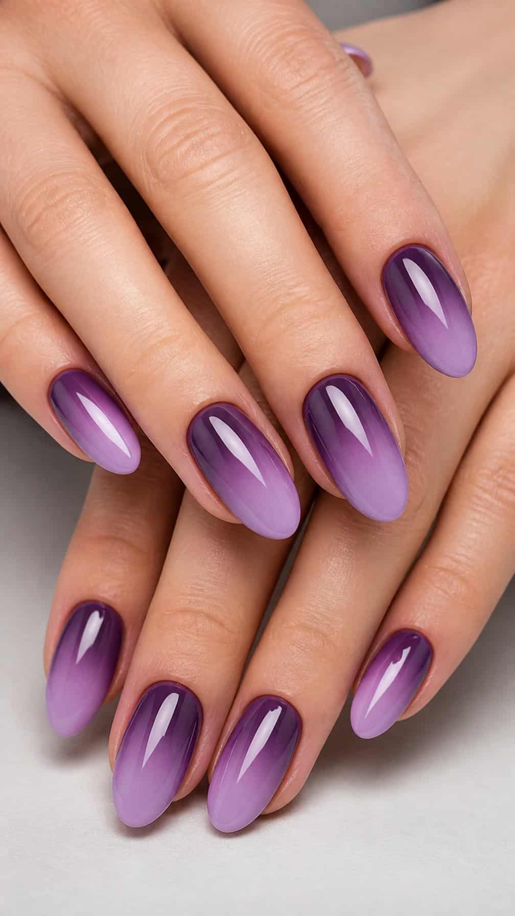 Close-up of hands with glossy nails fading from lilac to deep plum.