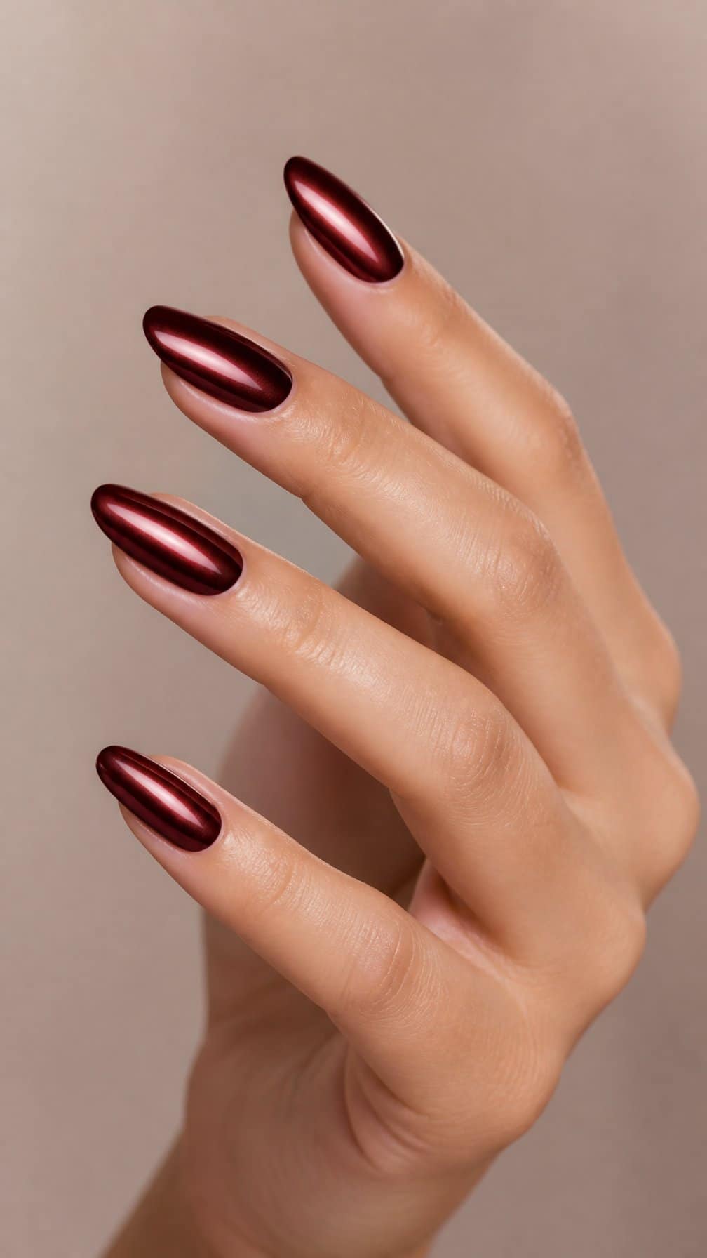 A hand displaying long almond-shaped maroon chrome nails against a neutral background.