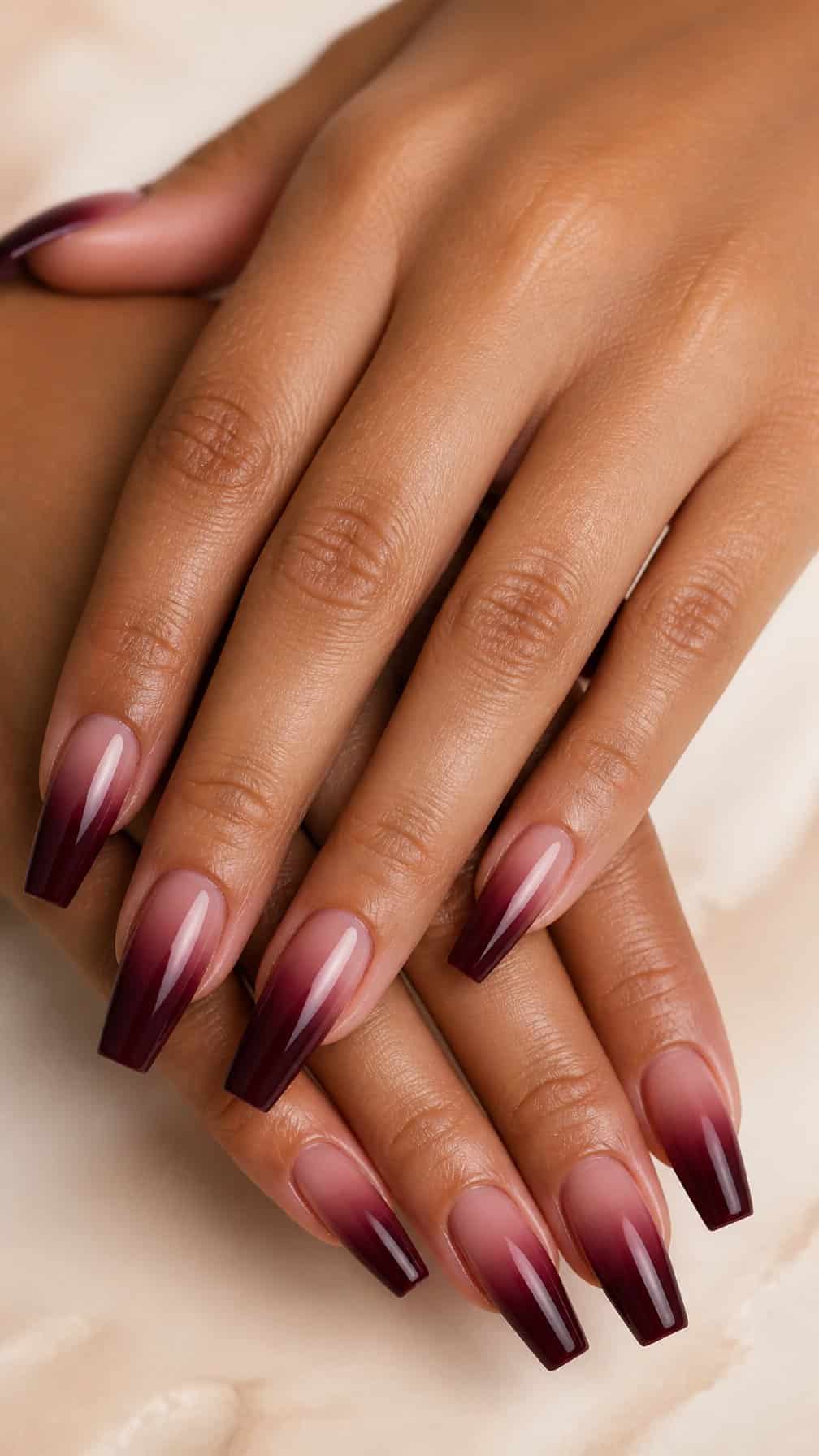 A hand with long coffin-shaped nails featuring a glossy maroon ombre manicure.