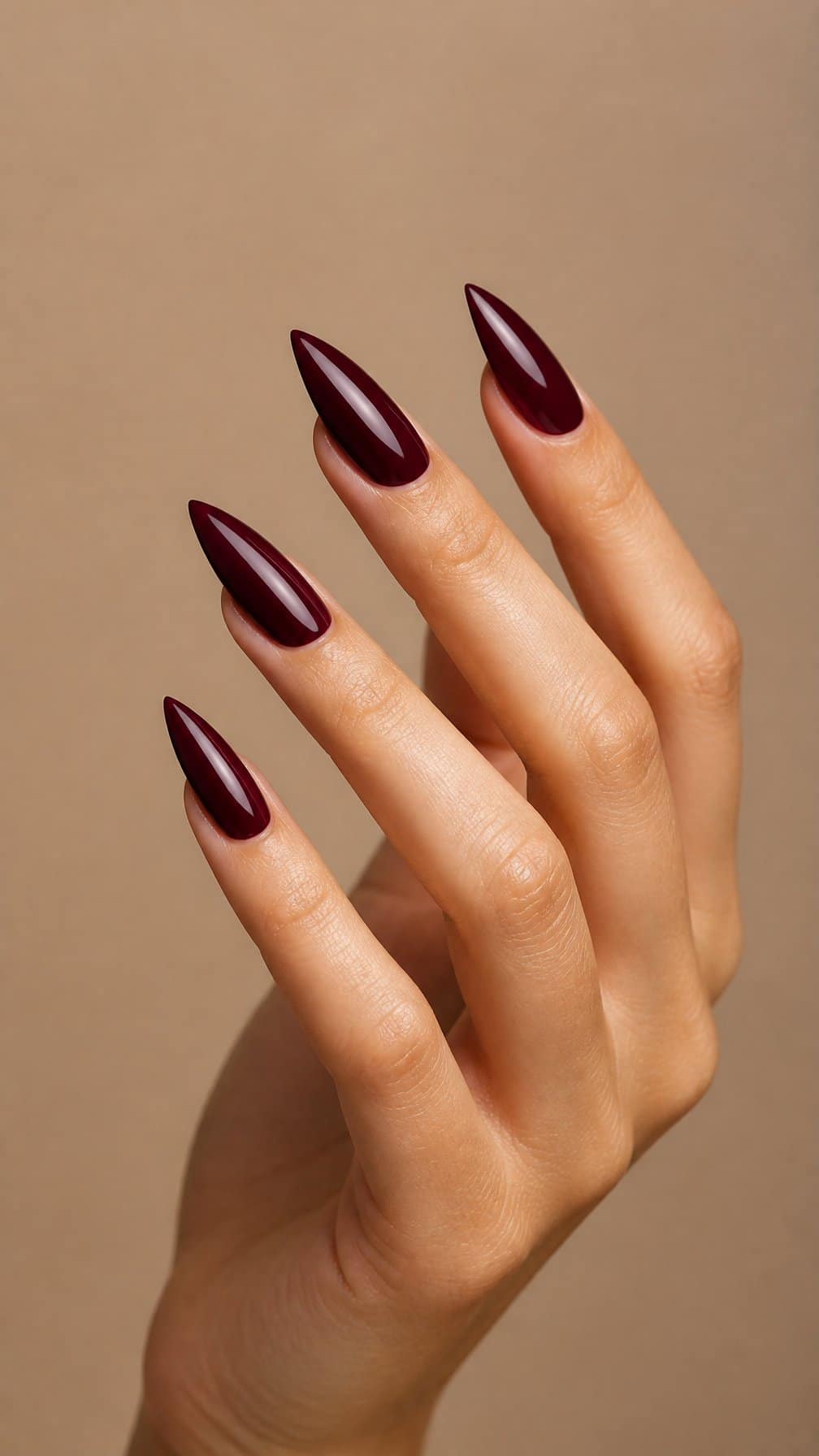 A hand with long, pointed nails painted glossy deep maroon.