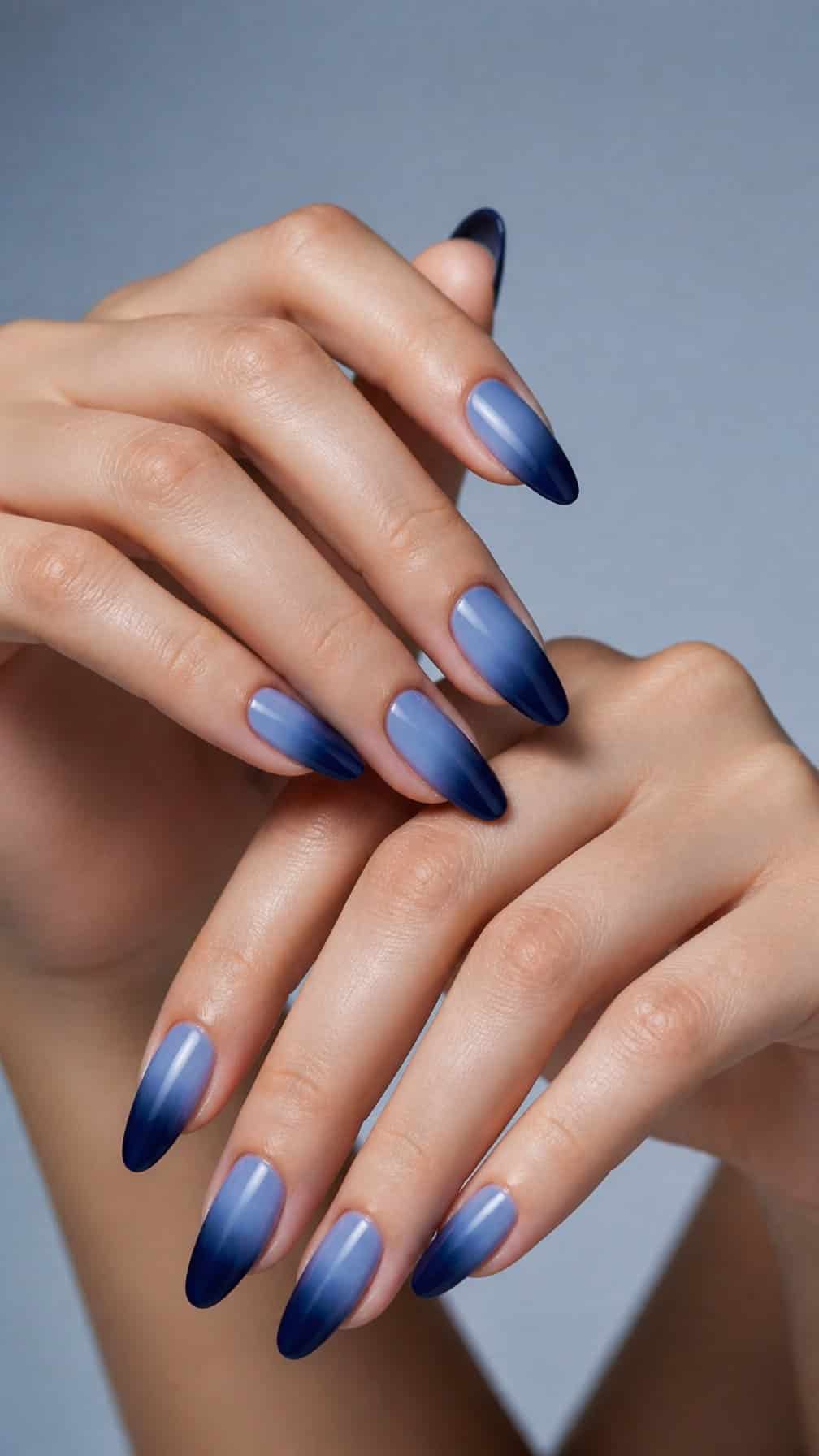A hand with almond-shaped nails painted in a navy blue to baby blue gradient.