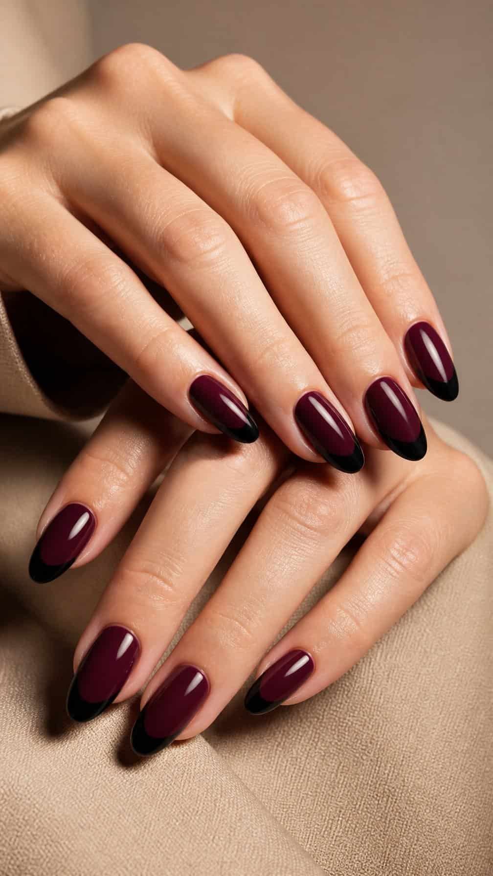 A close-up of manicured hands with deep plum nails and black French tips.