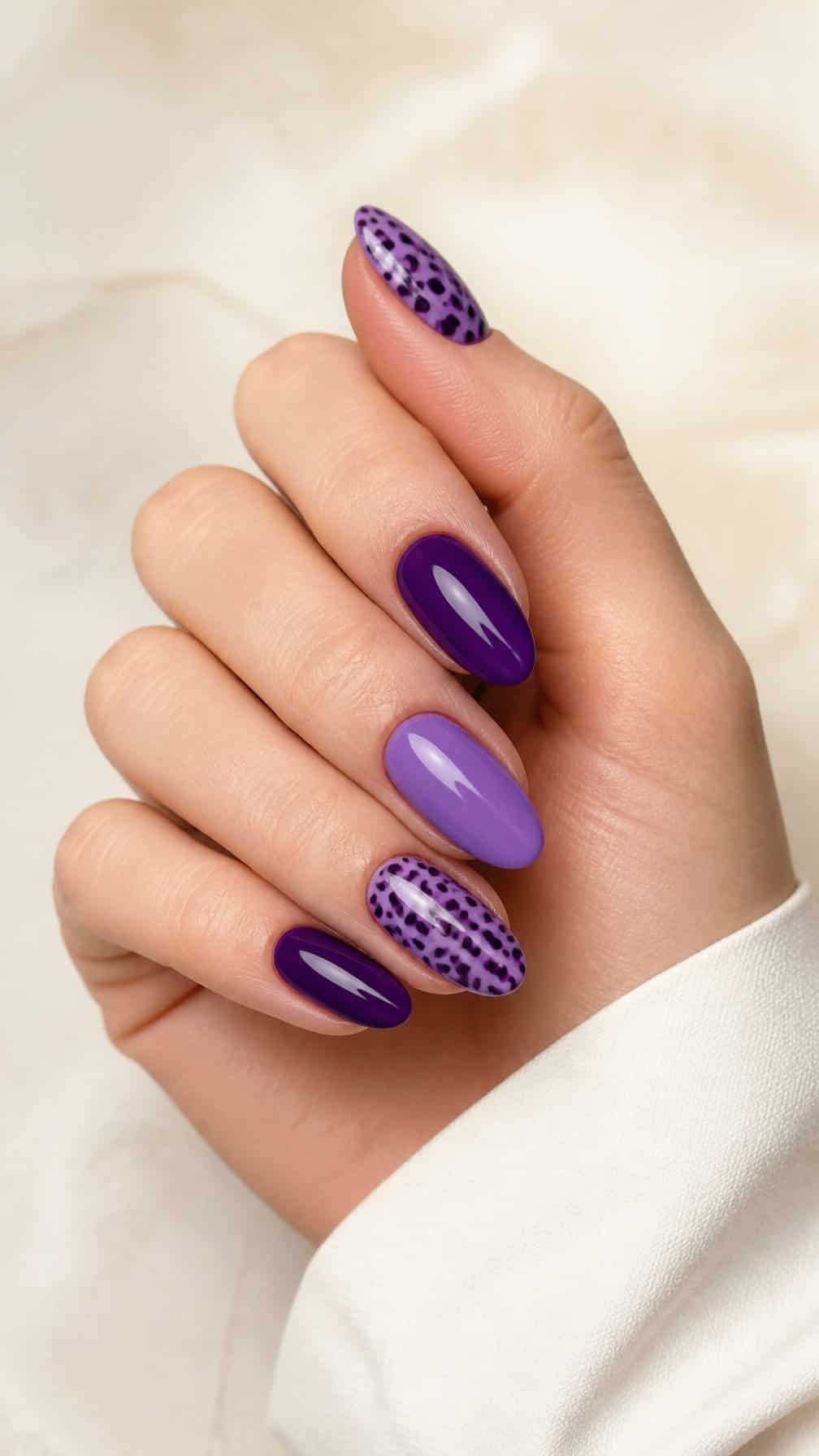 A hand displaying glossy purple nails with lilac and plum Dalmatian spots.