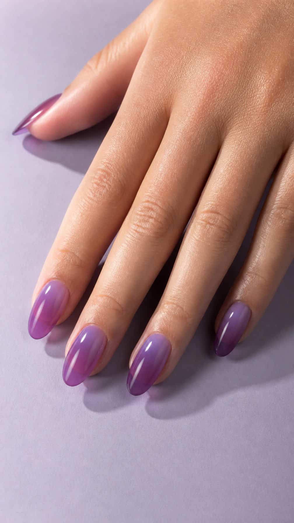 A manicured hand with glossy translucent purple nails resting on a pale lavender surface.