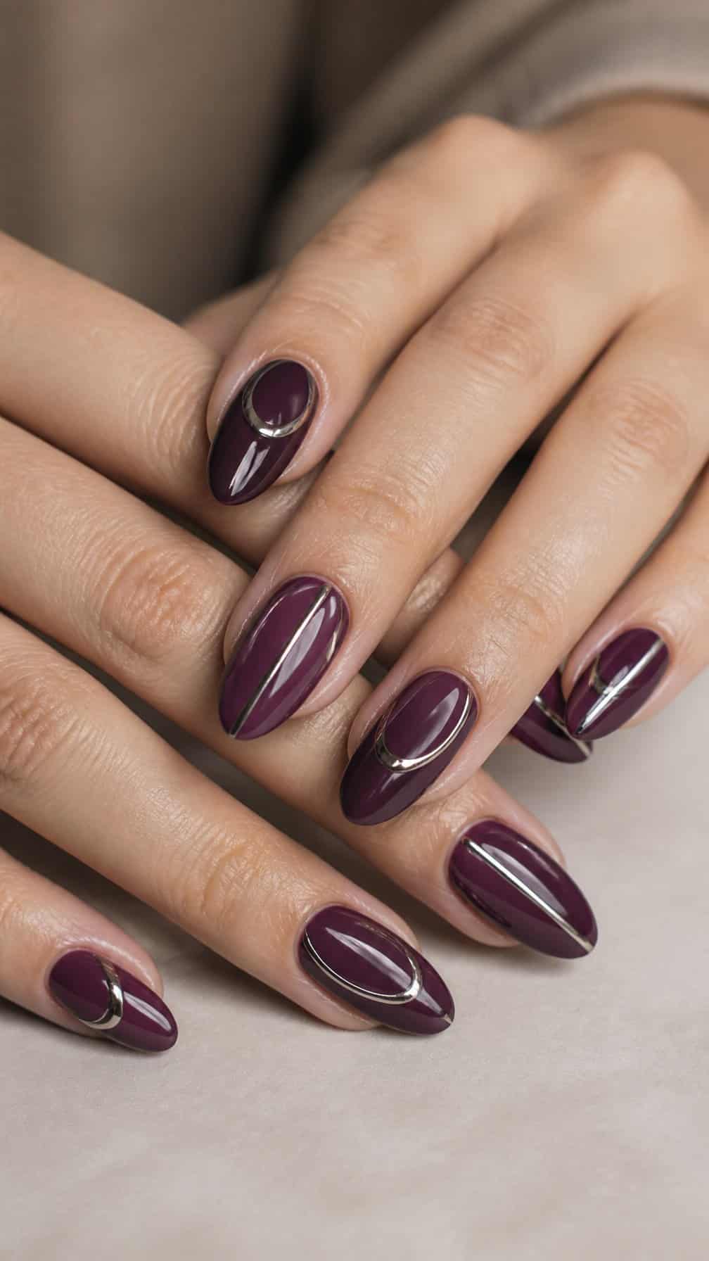 A close-up of almond-shaped raisin-purple manicured nails with thin chrome accent lines.