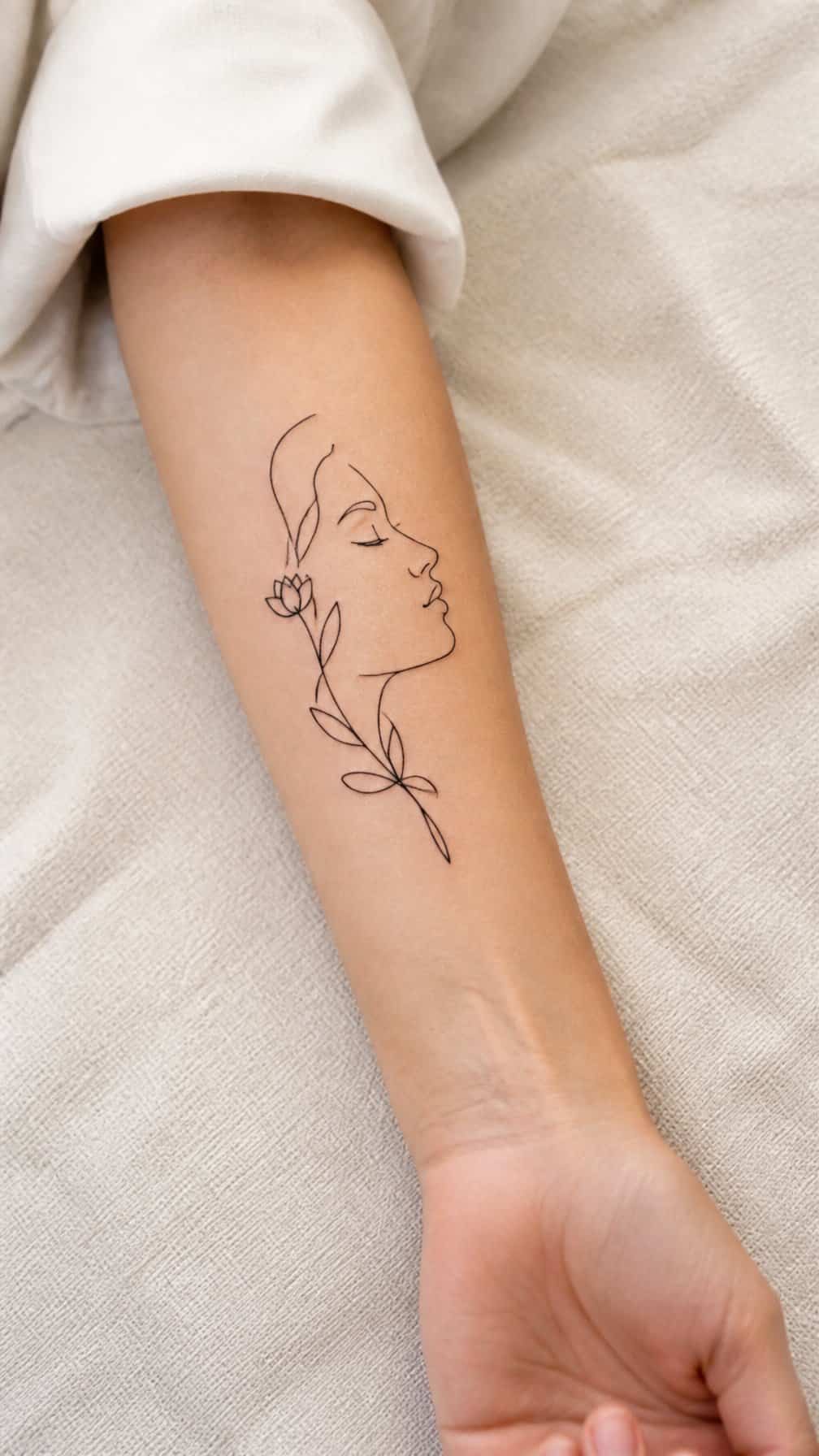 A woman’s forearm displaying a minimalist single-line profile tattoo.