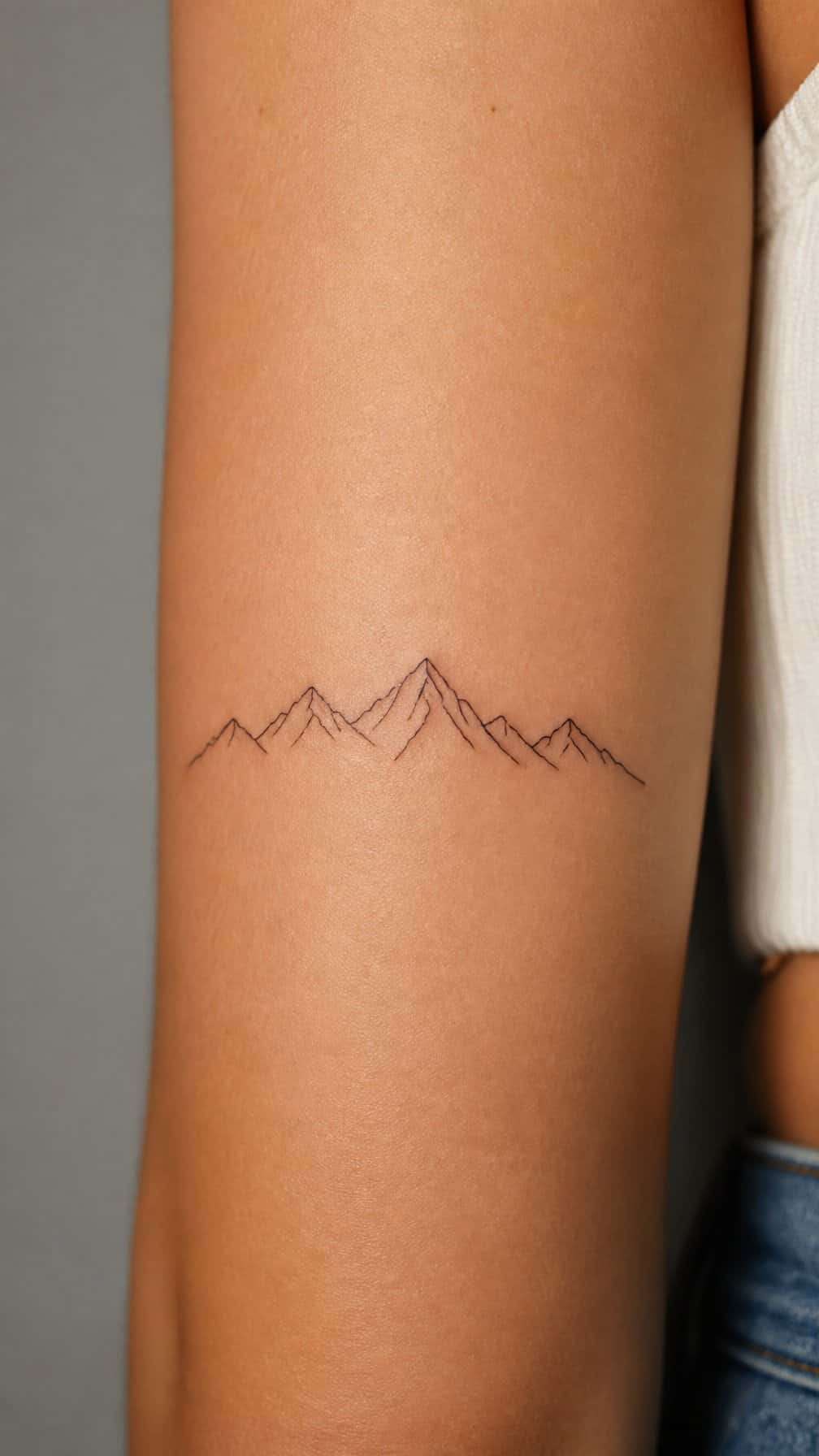 A simple continuous mountain range tattoo on natural skin.