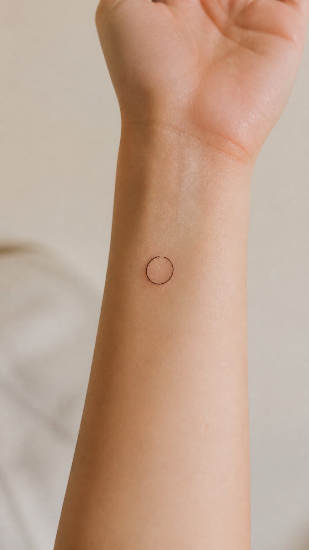 A close-up of a forearm with a small open circle tattoo.