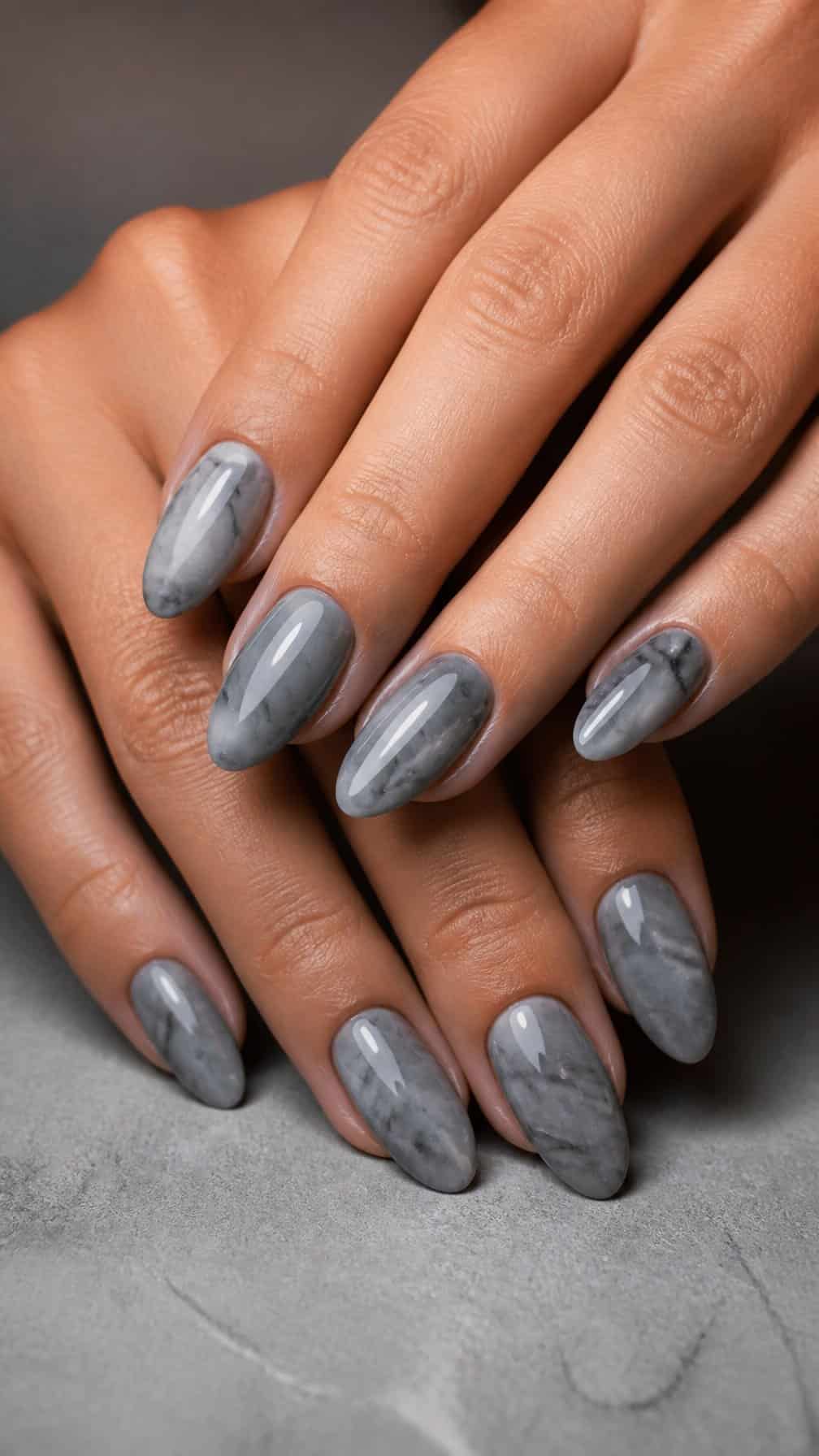 A close-up of hands with smoky gray marble-patterned manicure resting on a stone surface.