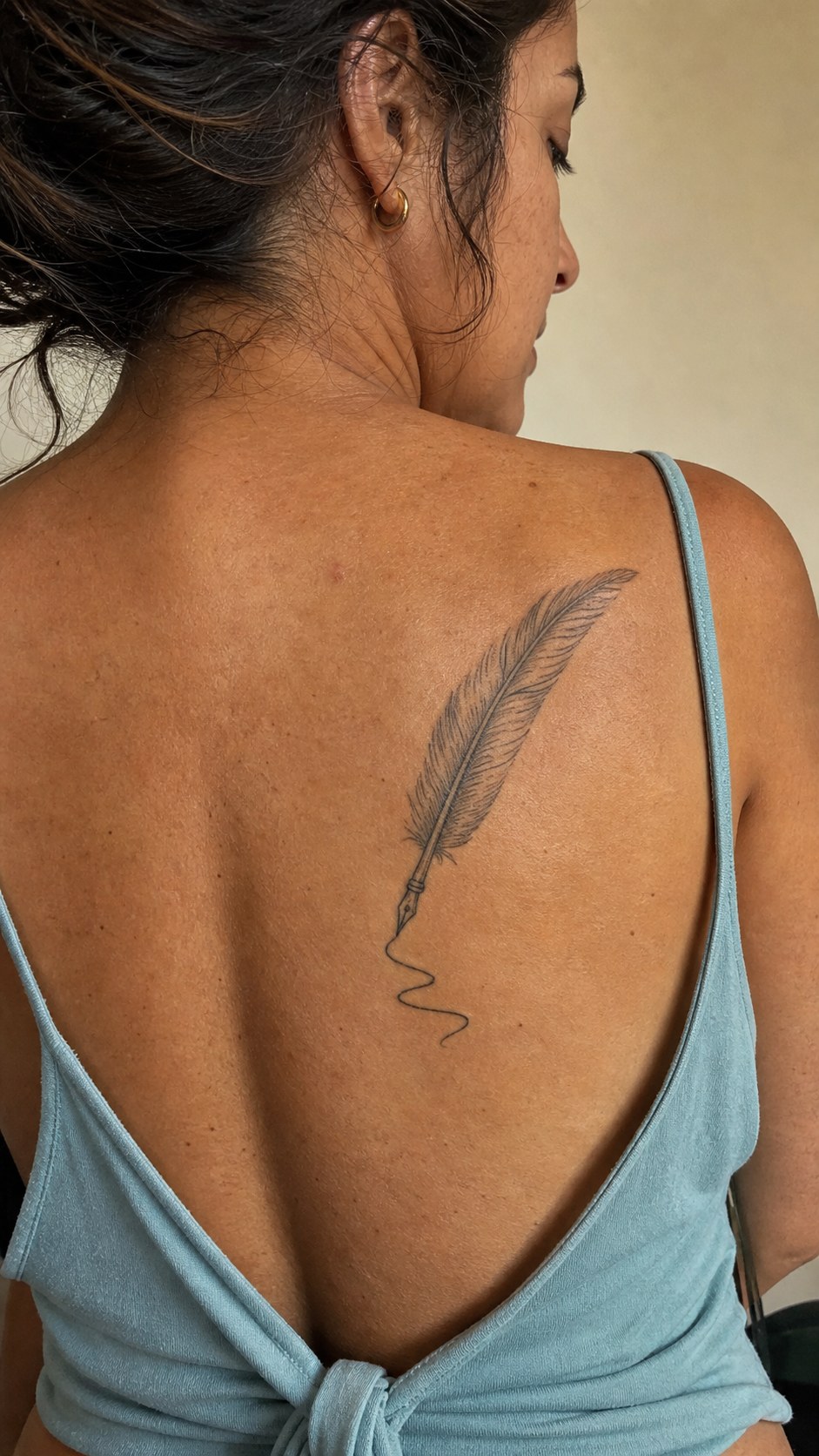 38 Creative Tattoo Ideas for Women 36 Healed feather quill tattoo on a adult woman's upper back, photographed in a natural relaxed documentary crop — study 2
