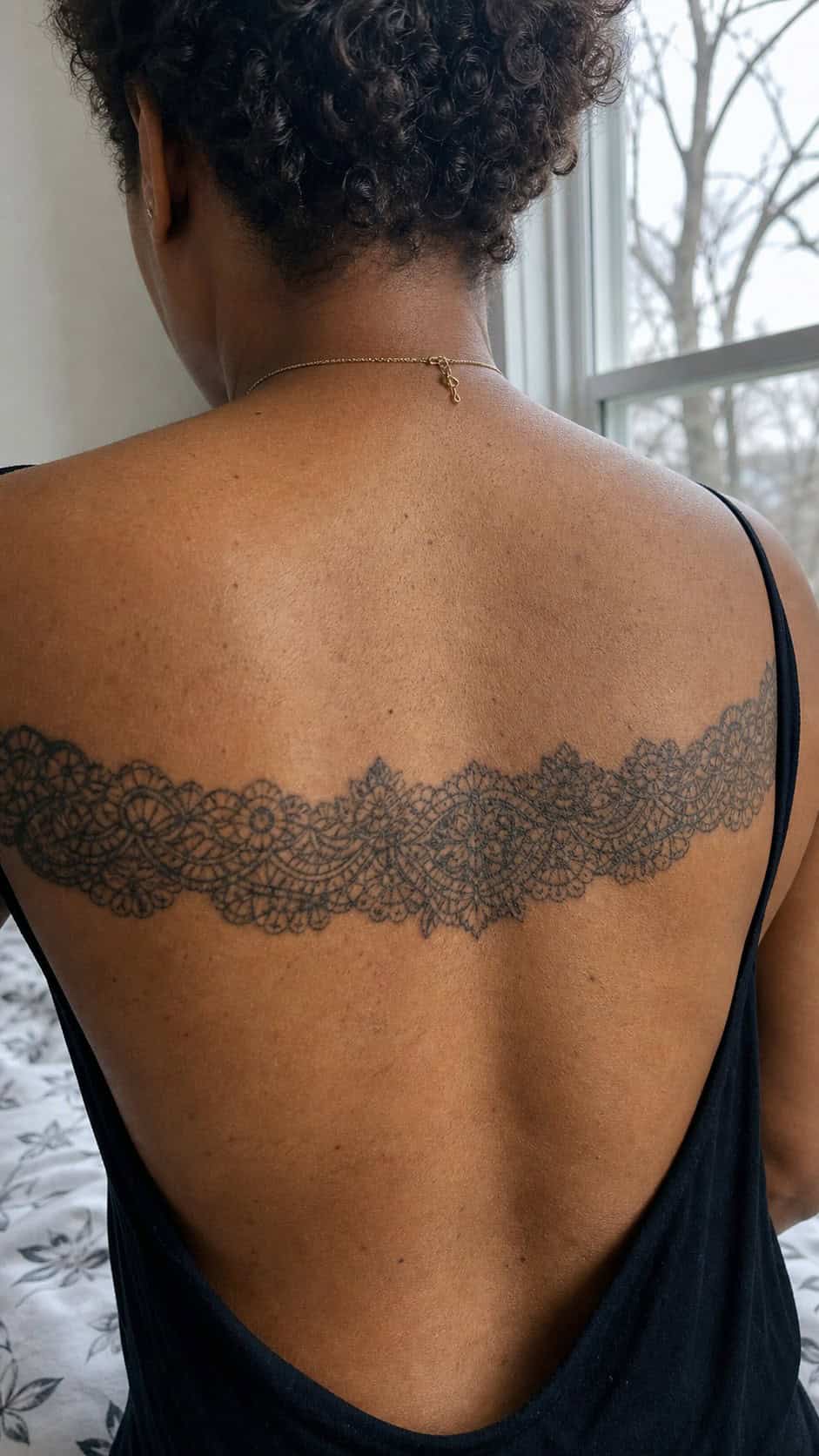 Healed intricate lace band tattoo on a adult woman's upper back, photographed in a natural slightly elevated close view — study 2