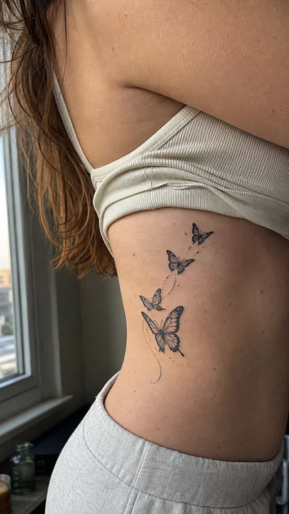 Healed butterfly flight tattoo on a adult woman's side ribs, photographed in a natural relaxed documentary crop — study 1