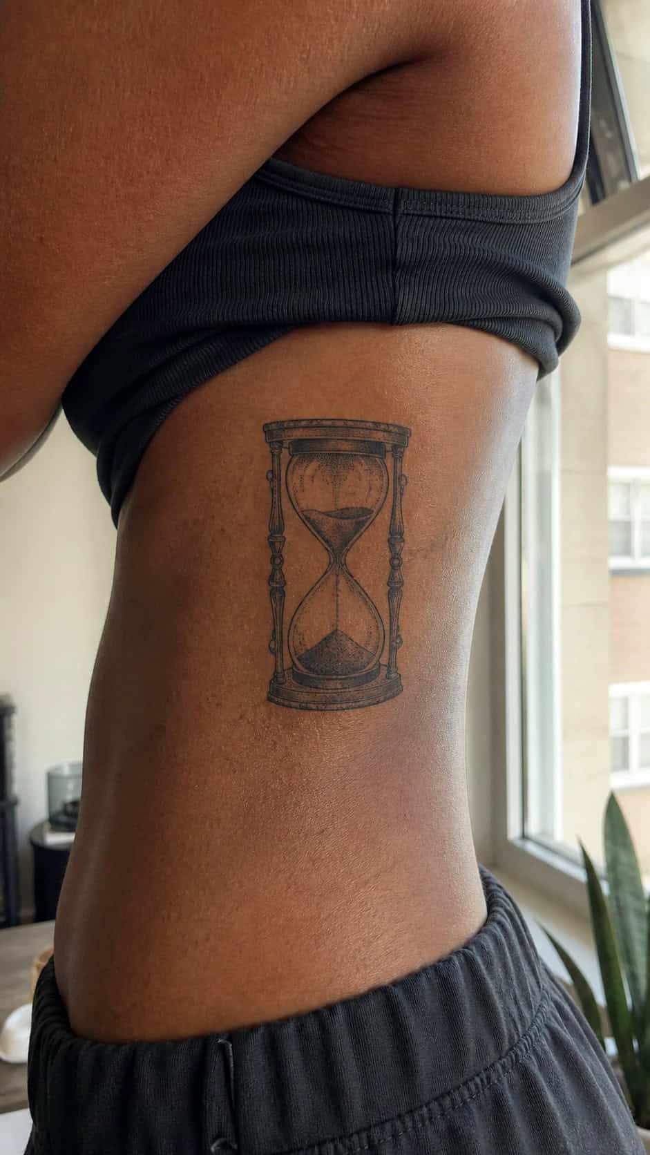 Healed hourglass tattoo on a adult woman's side ribs, photographed in a natural gentle side angle that clearly shows how the ink wraps — study 1